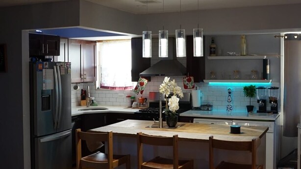 Una cocina moderna con una isla central, luces colgantes y un refrigerador.