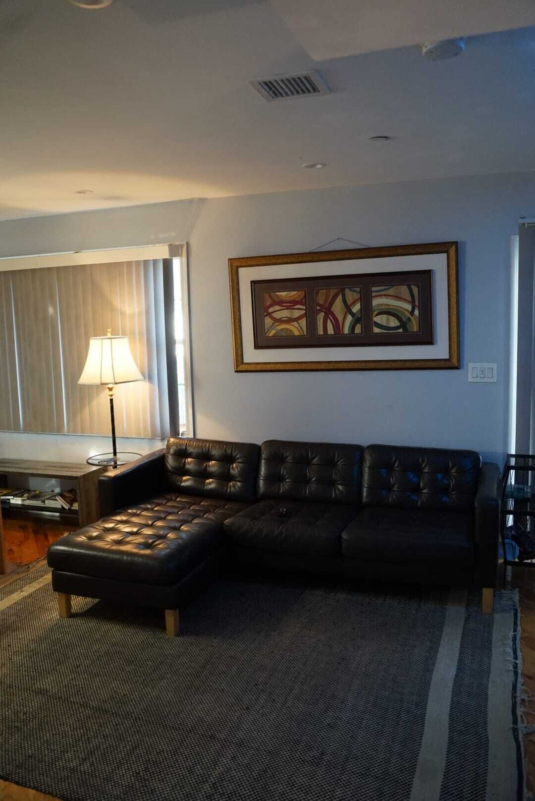 A living room with a sectional sofa, a floor lamp, and a framed abstract painting on the wall.
