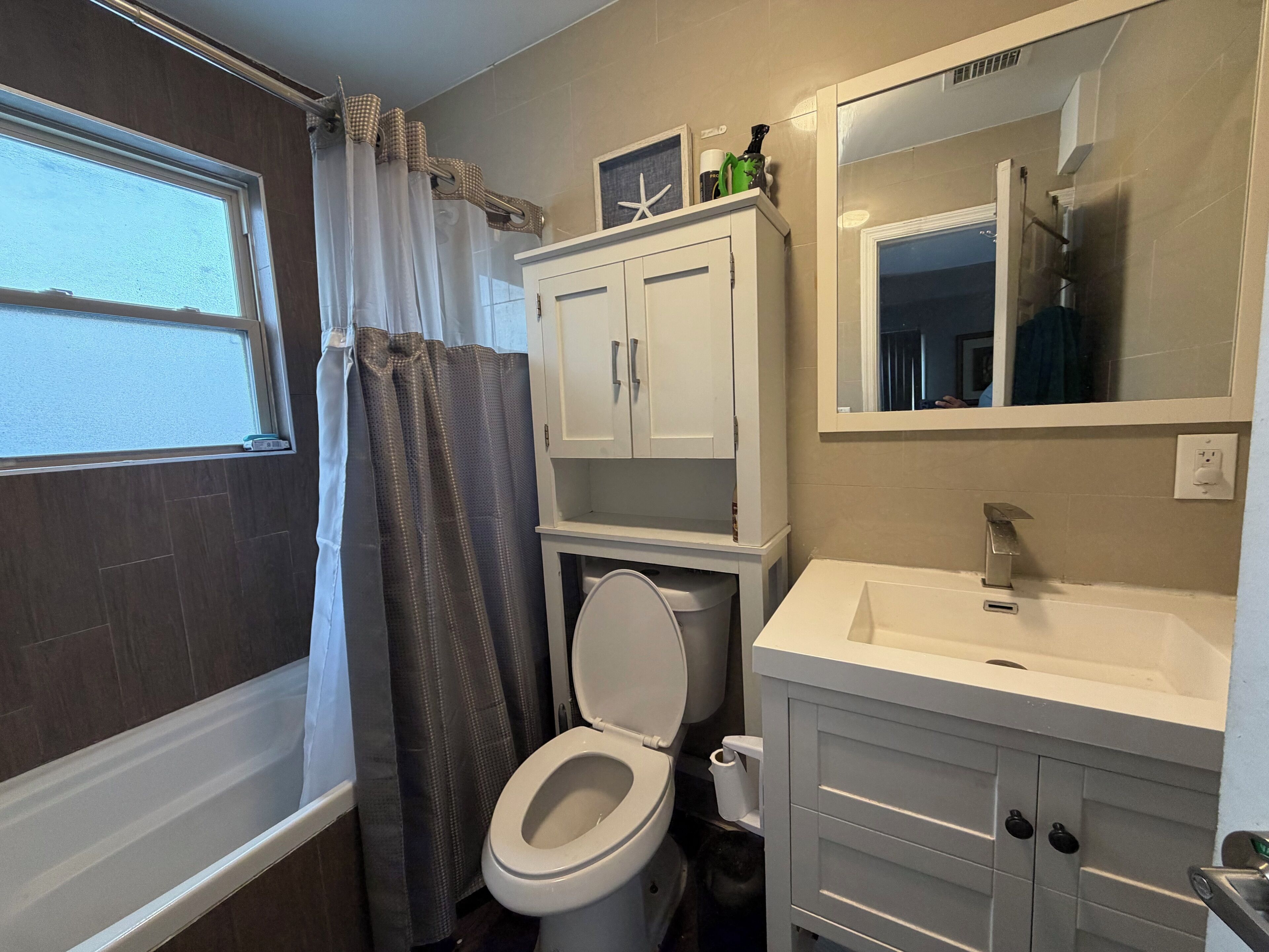 A bathroom with a toilet, a sink, a cabinet, and a shower curtain.