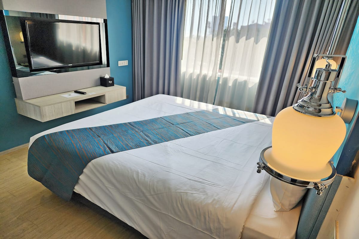 Een hotelkamer met een groot bed, een televisie op een standaard, een nachtkastje met een afstandsbediening en een raam met gordijnen.