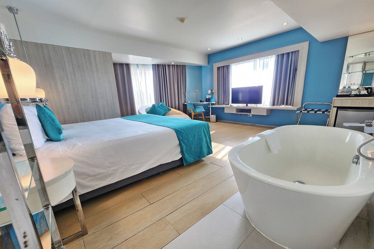 Een moderne hotelkamer met een groot bed, een zithoek, een badkuip en een bureau met een computer.