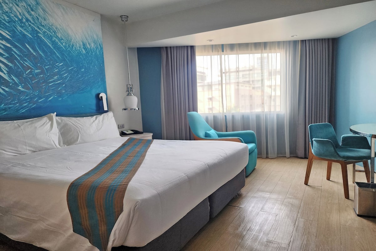 Een hotelkamer met een groot bed, een bureau, een stoel en uitzicht op de stad door het raam.