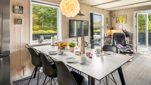 A modern dining area with a white table, black chairs, and a large window offering a view of greenery. - "Vilhelm" - 10km from the sea by Interhome (Oksbøl)