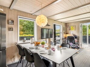 A modern dining area with a white table, black chairs, and a large window offering a view of greenery. - "Vilhelm" - 10km from the sea by Interhome (Oksbøl)