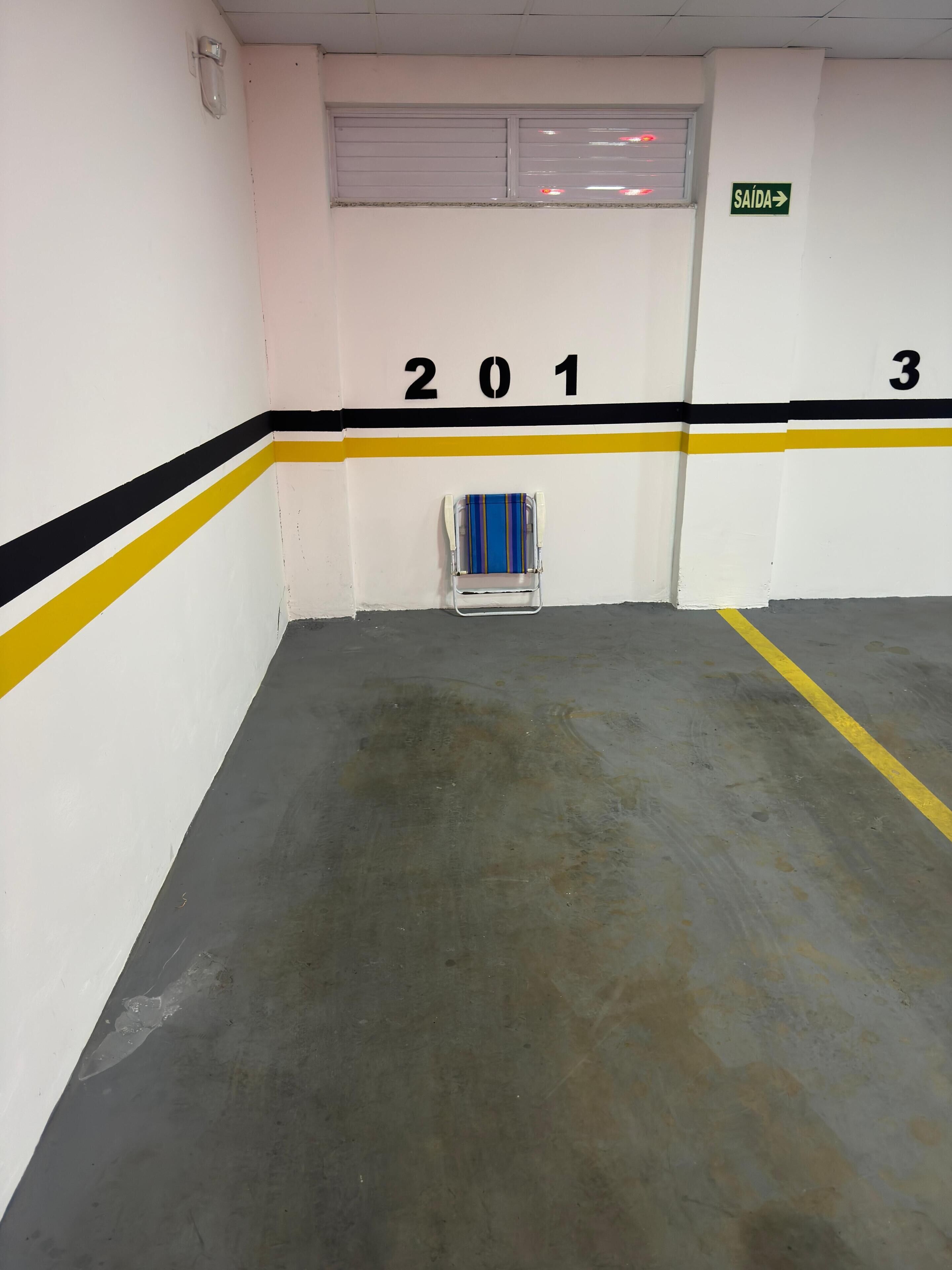 A parking garage with numbered parking spaces, a directional exit sign, and a chair in the center.