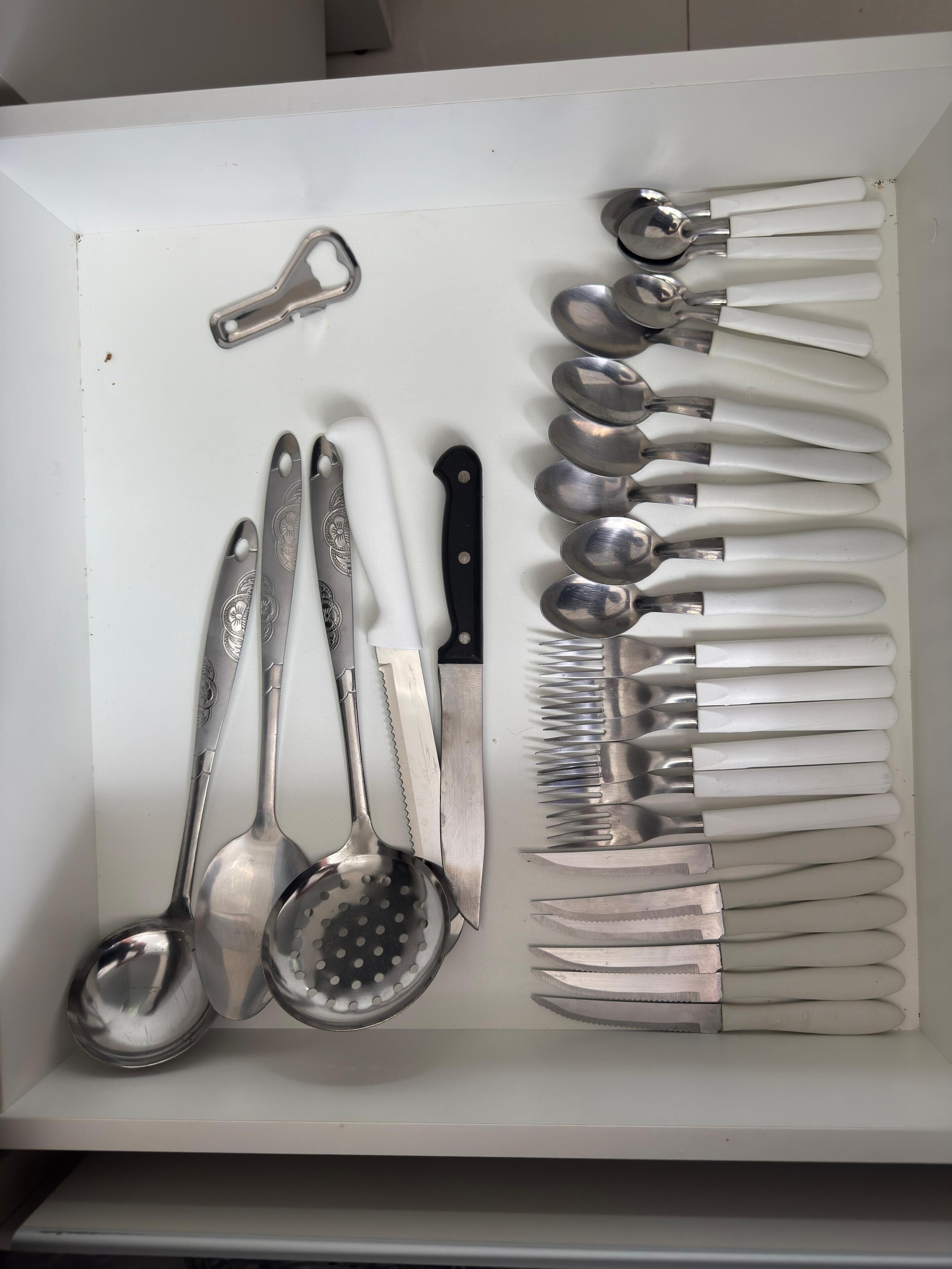 Un tiroir contenant divers ustensiles de cuisine, notamment des cuillères, des louches et une râpe.