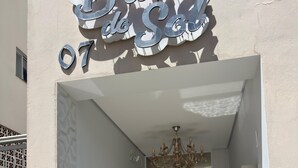 Entrada de hotel con diseño moderno, que incluye un patrón geométrico en la pared, una lámpara de araña y una puerta de cristal que da a la zona de recepción.