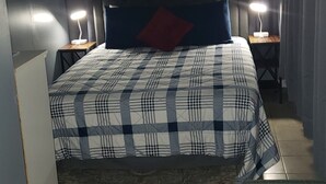 Un dormitorio con una cama, dos mesitas de noche con lámparas, una lámpara del techo y una pequeña mesa con una silla.