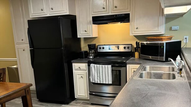 A kitchen with white cabinets, a black refrigerator, a stove, and a microwave. - centrally located 3 bed 2 bath (Albany)