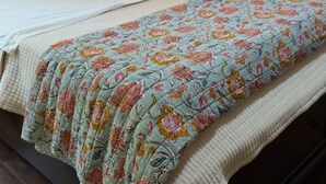 A neatly made bed with a floral quilt, a brown leather pillow, and a white pillow. There is a nightstand with a lamp and a window with curtains. - centrally located 3 bed 2 bath (Albany)