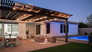 Una veranda coperta con piscina, mobili da esterno e un pergolato.