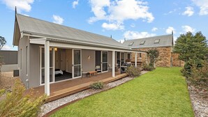 Une maison moderne dotée d’un patio couvert, avec un bâtiment en pierre en arrière-plan et une pelouse bien entretenue.