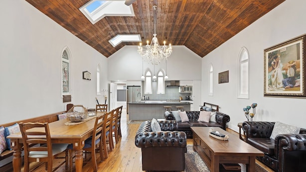 Un vaste salon doté d’un haut plafond, d’un plancher en bois, d’un coin repas avec des meubles en bois, d’un canapé en cuir et d’un lustre.