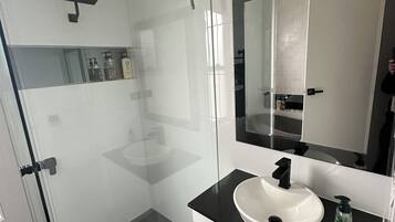 Ein modernes Badezimmer mit einer Duschkabine aus Glas, einem weißen Waschbecken mit schwarzer Arbeitsplatte und einem großen Spiegel darüber.