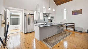 Une cuisine moderne dotée d’un îlot central, d’appareils électroménagers en acier inoxydable, de luminaires suspendus et d’un plafond en bois.