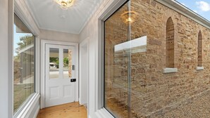 Un couloir doté d’un plancher en bois, d’une porte blanche avec un panneau de verre et d’un mur en pierre orné de fenêtres en arc de cercle.