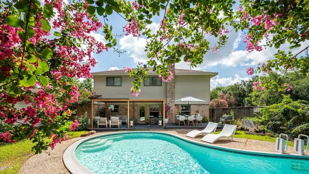 A swimming pool with lounge chairs, a covered patio with outdoor furniture, and a house in the background. - Peacock Paradise - Pool / Game (Houston)