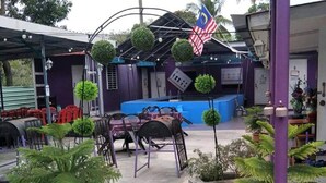 Un espacio al aire libre con mesas y sillas, rodeado de plantas en macetas y un pequeño césped.