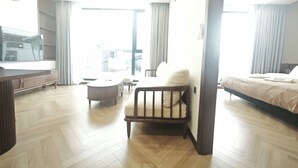 Amplia habitación de hotel con una cama grande, una silla de madera, una mesita redonda y un televisor.