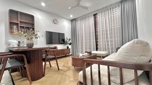 Una sala de estar moderna con una mesa de comedor de madera, sillas, un sofá, un televisor y un ventanal con cortinas.