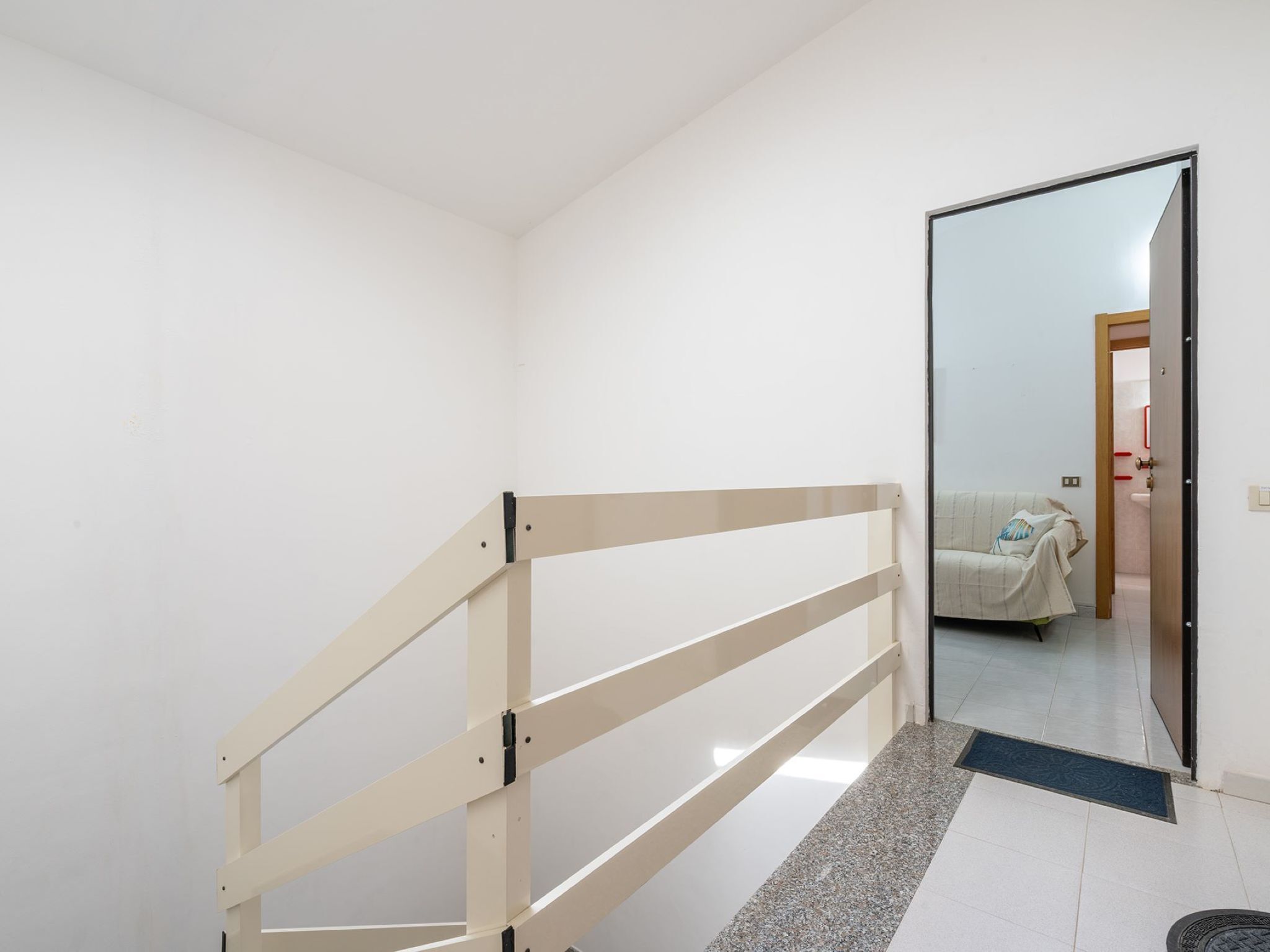 Een gang met houten leuning, een spiegelwand en een deur naar een kamer met een bed.