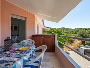 Ein Balkon mit Tisch für zwei Personen, einem Holzschrank und Blick auf grüne Hügel.