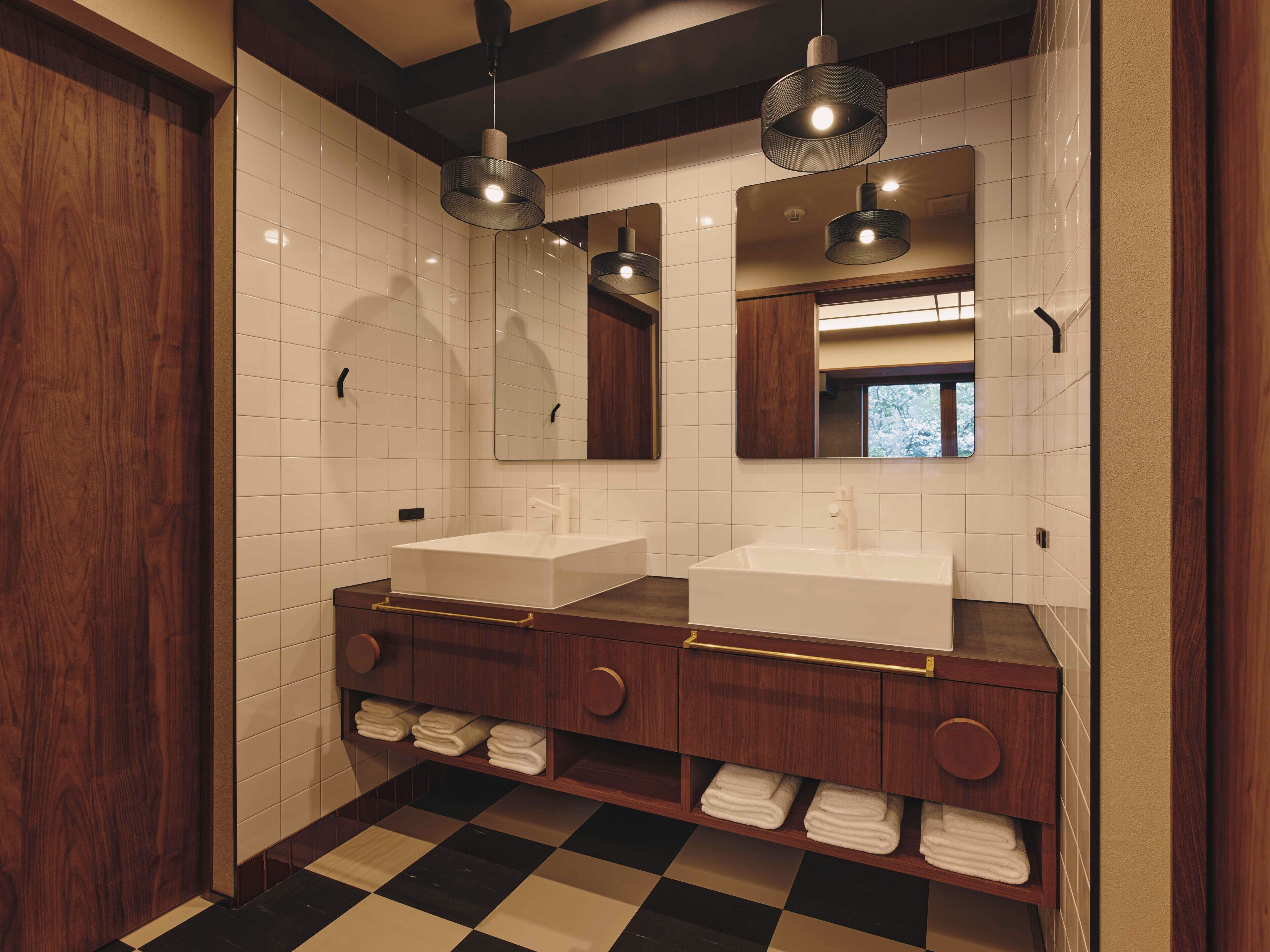 A modern bathroom with two sinks, wooden vanity, and checkered floor tiles.