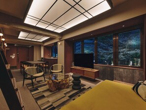 Un soggiorno moderno con una grande TV, mobili in legno e vista sulla città di notte.