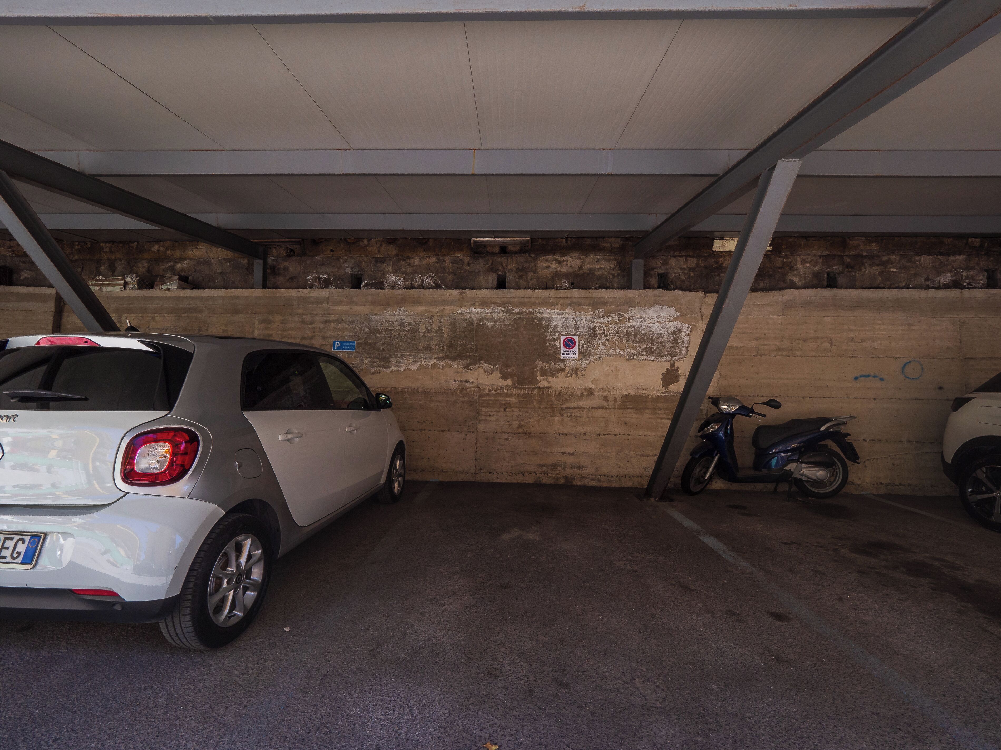 A parking garage with a white car and a motorcycle parked.