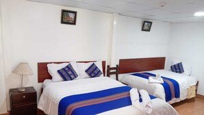 Camera d'albergo con due letti, ognuno con testiera in legno, biancheria da letto bianca e cuscini a motivi blu e bianchi. Un comodino con una lampada e un piccolo cassetto.