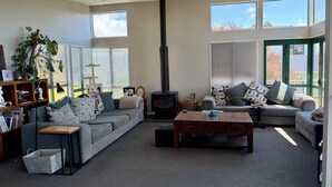 A modern living room with a sofa, a coffee table, a fireplace, and a bookshelf. - Beachlands Getaway - Room for everyone with a pool and views (Beachlands)