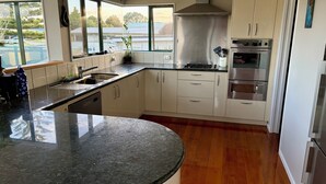 A modern kitchen with a curved granite countertop, stainless steel appliances, and a view of the outdoors through large windows. - Beachlands Getaway - Room for everyone with a pool and views (Beachlands)