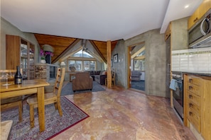 A spacious living area with a high ceiling, a dining table, and a kitchen area with modern appliances. - Fitzsimmons D - 3BR in the Heart of Whistler Village, Private Sauna (Whistler)
