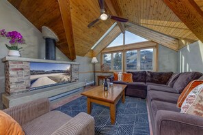 A cozy living room with a fireplace, a sofa set, and a view of a snowy landscape through large windows. - Fitzsimmons D - 3BR in the Heart of Whistler Village, Private Sauna (Whistler)