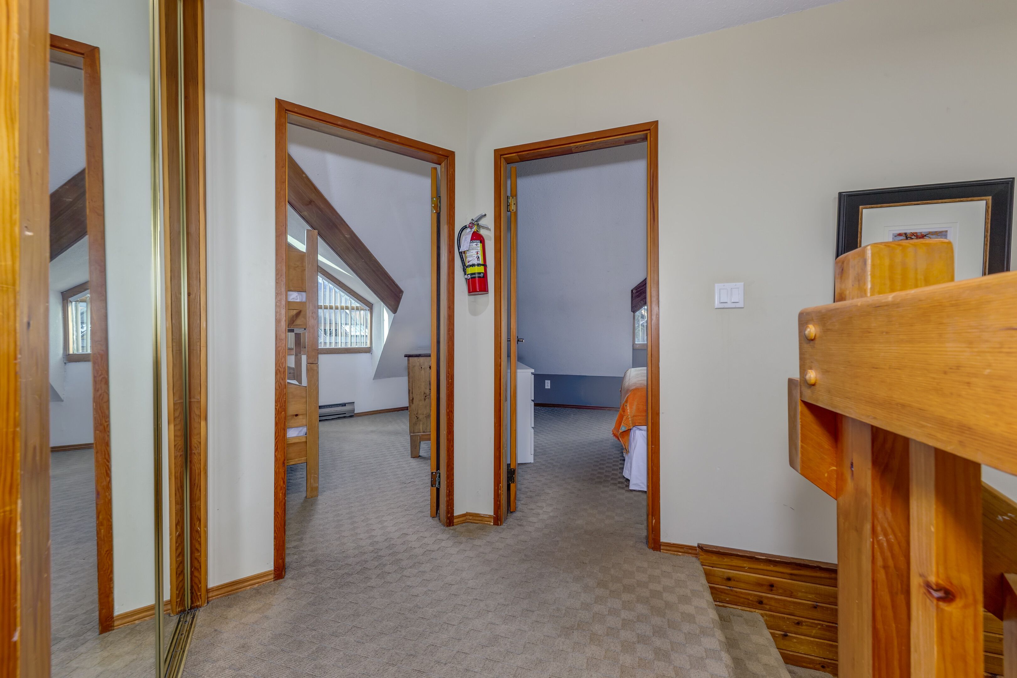 A hallway with wooden doors, a fire extinguisher, and a bed in the background.
