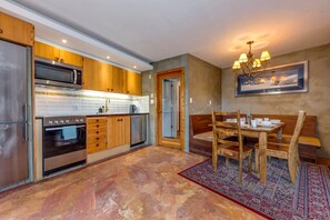 Une cuisine moderne avec des meubles en bois, des appareils électroménagers en acier inoxydable et un coin repas comprenant une table et des chaises en bois.