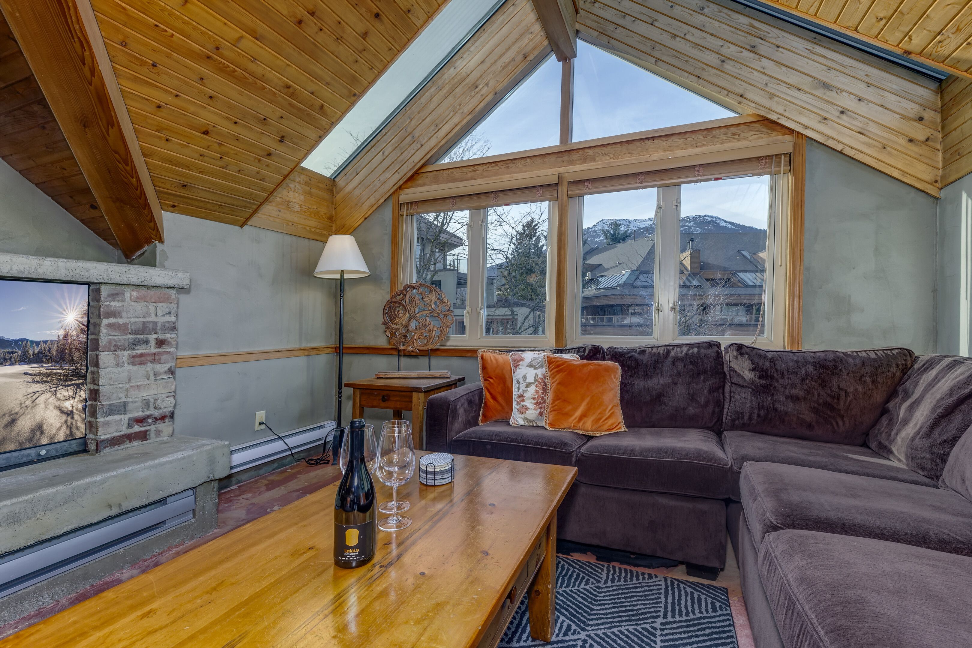 A cozy living room with a wooden ceiling, a fireplace, a sofa, and a table with a bottle and glasses.