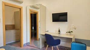 Une chambre d’hôtel avec un lit, un bureau, une chaise, une télévision, une valise et un miroir.
