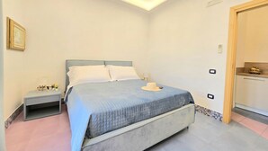 Une chambre à coucher avec un lit, des tables de chevet, une commode, un chapeau posé sur le lit et une porte donnant sur une salle de bain.