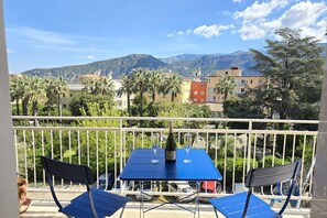 Ein Balkon mit Tisch und Stühlen mit Blick auf eine gebirgige Landschaft mit Gebäuden und Palmen.