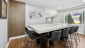 A modern kitchen with a large island, black bar stools, and a view of the outside. - Comfortable Luxurious 4BR Home w/ Game Room + Master Suite (Mount Prospect)