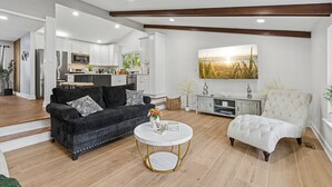 A modern living room with a dark sofa, a white armchair, and a round coffee table. - Comfortable Luxurious 4BR Home w/ Game Room + Master Suite (Mount Prospect)