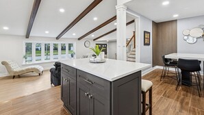 A spacious kitchen with a large island, dark cabinets, and a view of the outdoors through large windows. - Comfortable Luxurious 4BR Home w/ Game Room + Master Suite (Mount Prospect)
