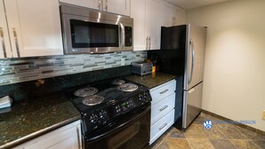 A modern kitchen with stainless steel appliances, white cabinets, and a tiled backsplash. - Slopeside Penthouse Apartment with Pool, Hot Tub and Sauna (Whistler)