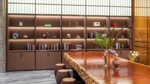 A modern interior with a wooden bookshelf, a polished wooden table, and a seating area with patterned stools. - ECHENG Liuzhou Wuxing Buxingjie (Liuzhou)