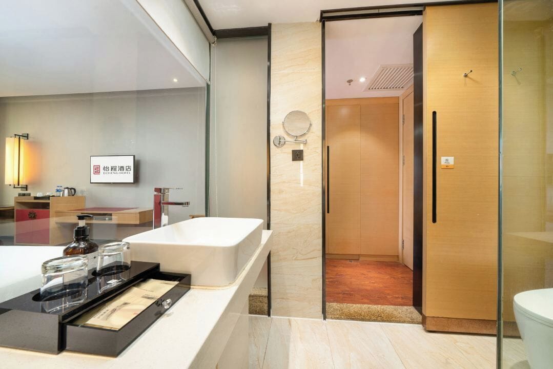 A modern bathroom with a large mirror, a sink, and a toilet. There is a wooden door and a glass partition.