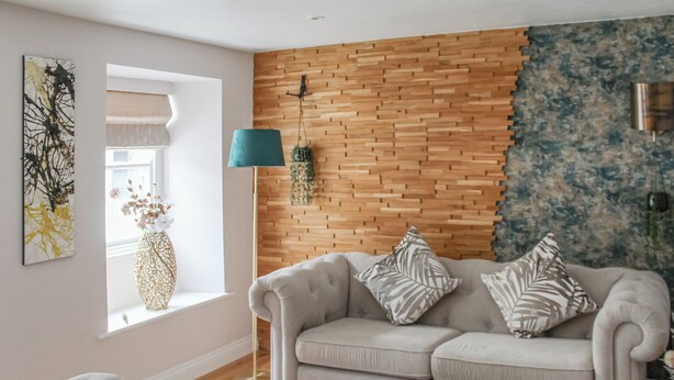 Un soggiorno con un divano grigio, una parete decorata in legno, una finestra con tenda bianca e una lampada da terra.