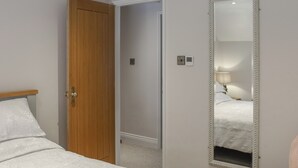 Una camera da letto con una porta in legno, un letto con biancheria bianca, un grande specchio e un comodino con una lampada.