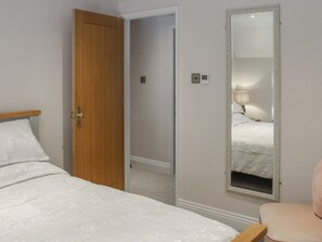 A bedroom with a wooden door, a bed with white bedding, a large mirror, and a small bedside table with a lamp. - The Cottage - UK50652 (Falmouth)