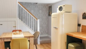 Una cucina compatta con un tavolo di legno, una sedia gialla, un frigorifero bianco e una scala che conduce in un'altra stanza.